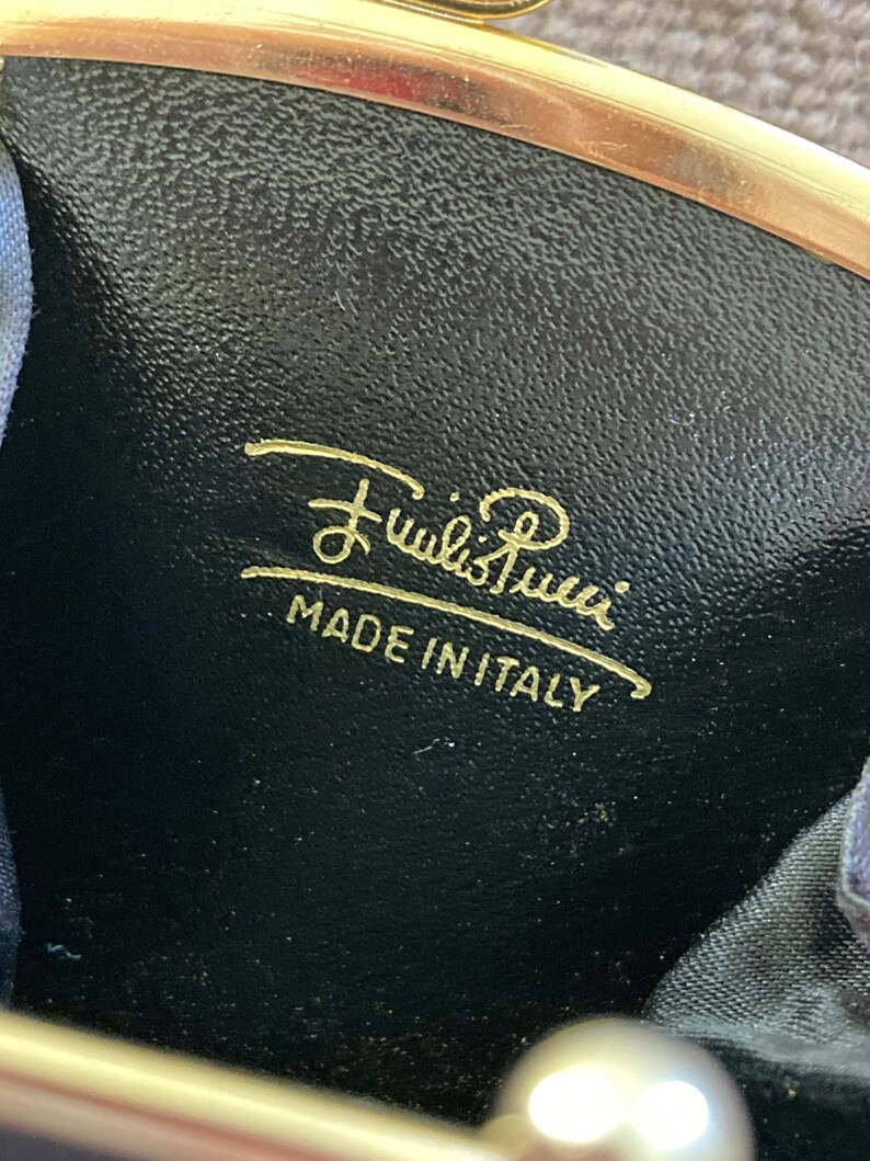 May include: A black leather coin purse with gold-toned hardware and the inscription "Furla's Roma" in gold lettering. The purse also has the text "Made in Italy" in gold lettering.