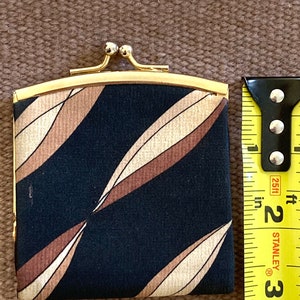 May include: A small black and brown patterned coin purse with a gold metal frame and clasp. The purse is about 3 inches wide and 2 inches tall.