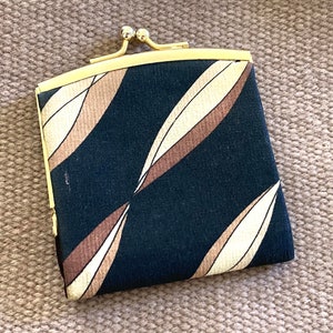 May include: A small black fabric coin purse with a gold metal frame and clasp. The fabric has a pattern of brown and cream colored leaves.