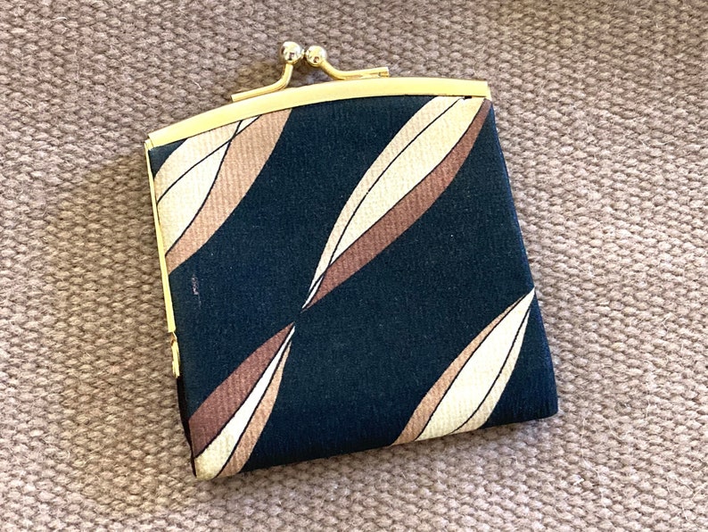 May include: A small black fabric coin purse with a gold metal frame and clasp. The fabric has a pattern of brown and cream colored leaves.