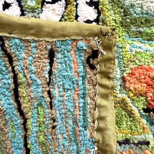 May include: Close-up of a colorful rug with a green, blue, and orange pattern. The rug has a green fabric border with a white stitching detail.