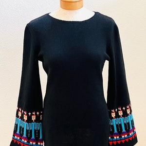 May include: Black long-sleeve sweater with a ribbed texture and colorful embroidered figures on the cuffs.