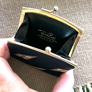 May include: A black and gold coin purse with a geometric pattern. The purse is open and the inside is lined with black fabric. The purse has a gold clasp and the words "Emilio Pucci MADE IN ITALY" are printed on the inside.