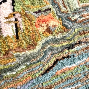 May include: Close-up of a colorful, textured rug with a variety of shades of green, brown, blue, and orange. The rug is made of looped yarn and has a unique, hand-crafted look.