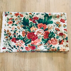 May include: A white fabric with a floral pattern featuring pink, red, and green flowers. The fabric has a vintage feel and would be perfect for crafting projects.