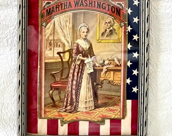 May include: Framed image of Martha Washington in a red, white, and blue frame. The image shows Martha Washington standing in a room with a chair, a table, and a basket of fruit. The text "MARTHA WASHINGTON" is written in a banner above her head.