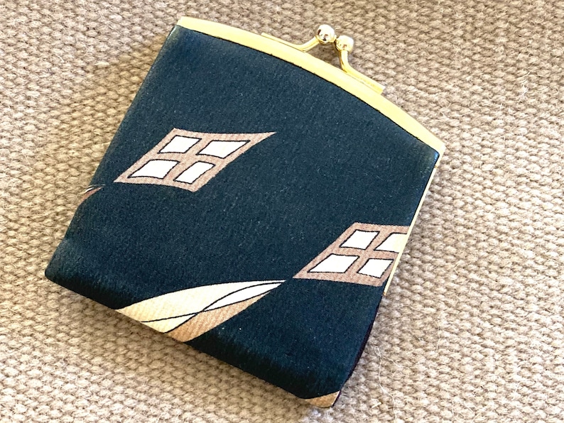 May include: A small, dark green coin purse with a gold clasp and a geometric pattern of white and brown diamonds.