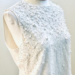 May include: A white sleeveless dress with a pearl embellishment on the bodice.