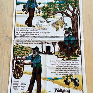 May include: A white tea towel with a colorful illustration of a swagman singing the Australian folk song "Waltzing Matilda". The lyrics of the song are printed on the tea towel, along with a glossary of Australian slang terms. The tea towel is designed in Australia by Buck Marketing.