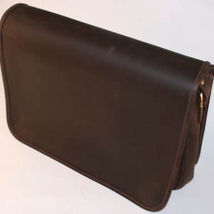 May include: A brown leather messenger bag with a flap closure and a gold metal buckle. The bag has a zippered pocket on the front and a strap for carrying.