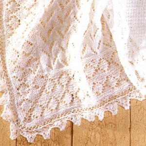 May include: A white crocheted shawl with a delicate lace pattern. The shawl is folded and draped over a wooden surface.