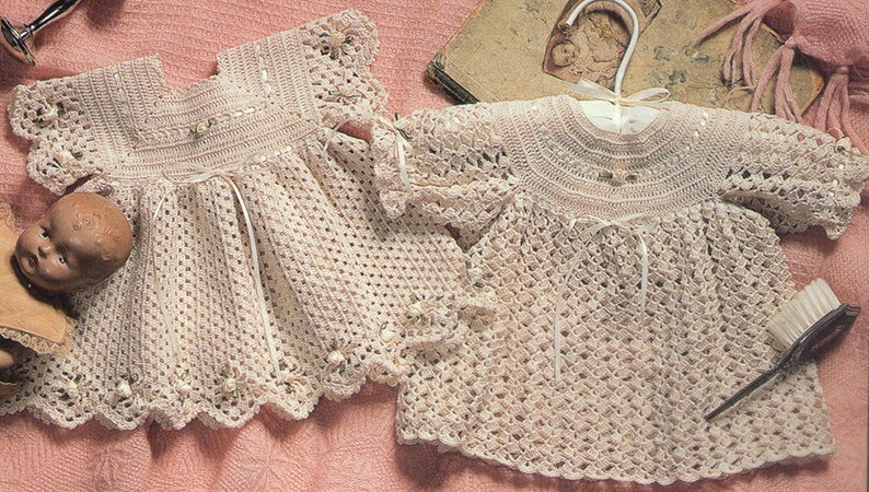 May include: Two crocheted baby dresses in a cream color. The dresses have a delicate lace trim and are made with a fine yarn.