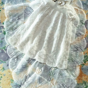 May include: Two white crocheted baby blankets with delicate lace patterns. The top blanket is folded over the bottom blanket. A small silver box and two silver rings are on top of the blankets.