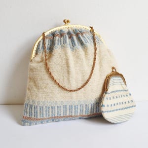 May include: A vintage handbag and matching coin purse. The bag is cream-colored with blue and brown accents, a gold clasp, and a chain handle. The coin purse has a similar design.