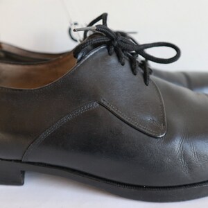 May include: A pair of black leather dress shoes with laces. The shoes have a classic design with a rounded toe and a low heel. The leather appears to be smooth and polished, and the laces are black.