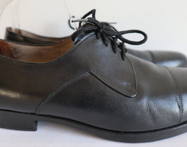 May include: A pair of black leather dress shoes with laces. The shoes have a classic design with a rounded toe and a low heel. The leather appears to be smooth and polished, and the laces are black.