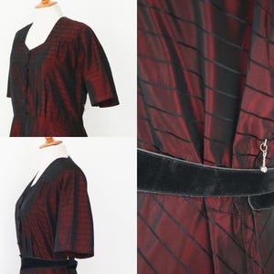 May include: A vintage dress in a deep burgundy and black striped pattern. The dress features short sleeves, a V-neck, and a black velvet belt. The fabric has a subtle sheen, and the dress is displayed on a mannequin.