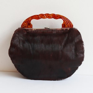 Puede incluir: Un bolso vintage con cuerpo de piel marrón oscuro y asa con estampado de carey. El bolso tiene forma redondeada y cierre metálico. El asa es curva y tiene un diseño trenzado.