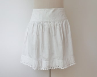 May include: A white, gathered skirt with a scalloped hem. The skirt has a high waist and a flared silhouette. The fabric appears to be cotton or a similar lightweight material. The skirt is displayed on a mannequin.