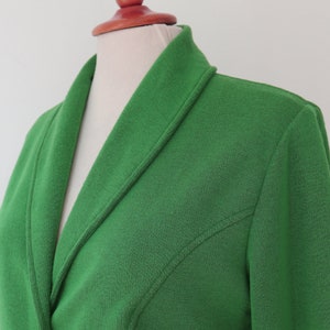 May include: A bright green blazer featuring a shawl collar and a textured fabric finish. The garment includes long sleeves and visible seam detailing that runs diagonally from the armhole towards the centre front, creating a structured appearance.