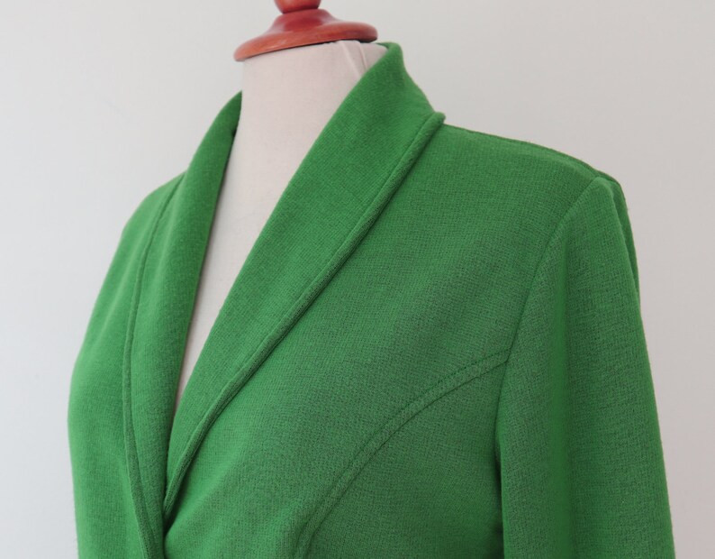 May include: A bright green blazer featuring a shawl collar and a textured fabric finish. The garment includes long sleeves and visible seam detailing that runs diagonally from the armhole towards the centre front, creating a structured appearance.