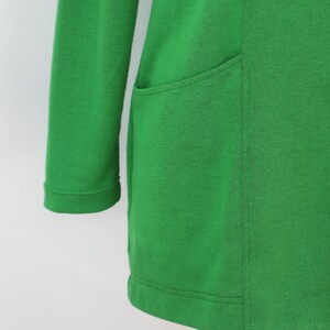 May include: A vibrant green long-sleeved cardigan featuring a smooth knit texture, a straight hemline, and two visible matching green buttons on the front placket. The garment includes a single patch pocket on the side with clean stitched seams.