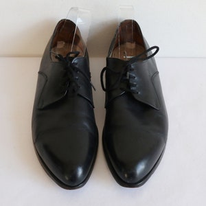 May include: A pair of black leather dress shoes with laces. The shoes have a classic design with a pointed toe and a low heel. The shoes are displayed on a white surface.