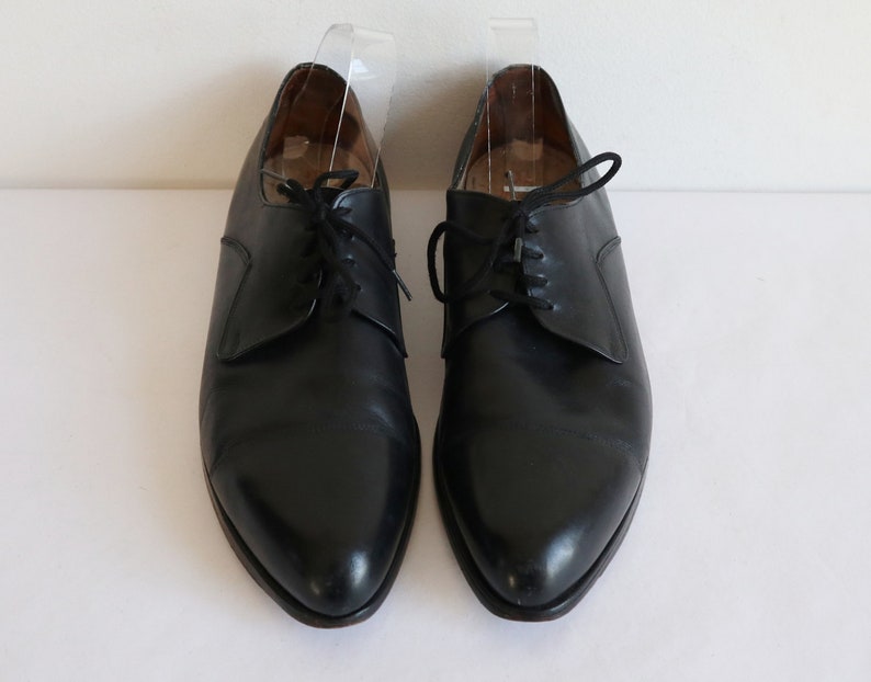 May include: A pair of black leather dress shoes with laces. The shoes have a classic design with a pointed toe and a low heel. The shoes are displayed on a white surface.