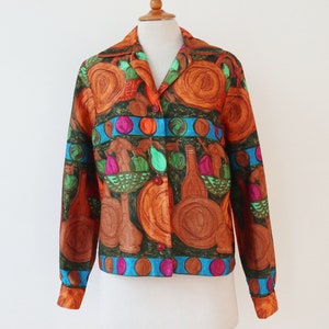 May include: A button-down shirt with a vibrant, artistic print. The design features brown, orange, and green illustrations of bottles, fruit baskets, and plates, accented with blue and pink details. The shirt is displayed on a mannequin.
