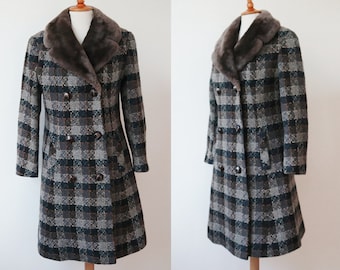 Op de afbeelding: Een vintage double-breasted jas met een ruitpatroon in tinten grijs, bruin en blauwgroen. De jas heeft een imitatiebontkraag en donkerbruine knopen. De jas wordt gepresenteerd op een houten mannequin.