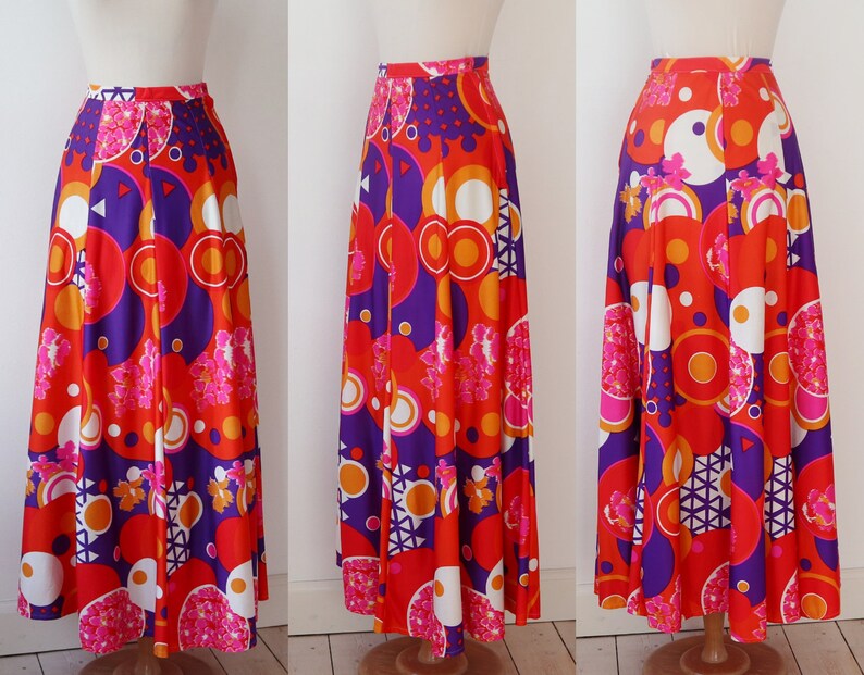 May include: A long, flowing skirt with a vibrant, retro-inspired print. The skirt features a bold pattern of red, orange, purple, white, and pink geometric shapes and floral accents. The skirt is displayed on a mannequin, showcasing its full length and design.
