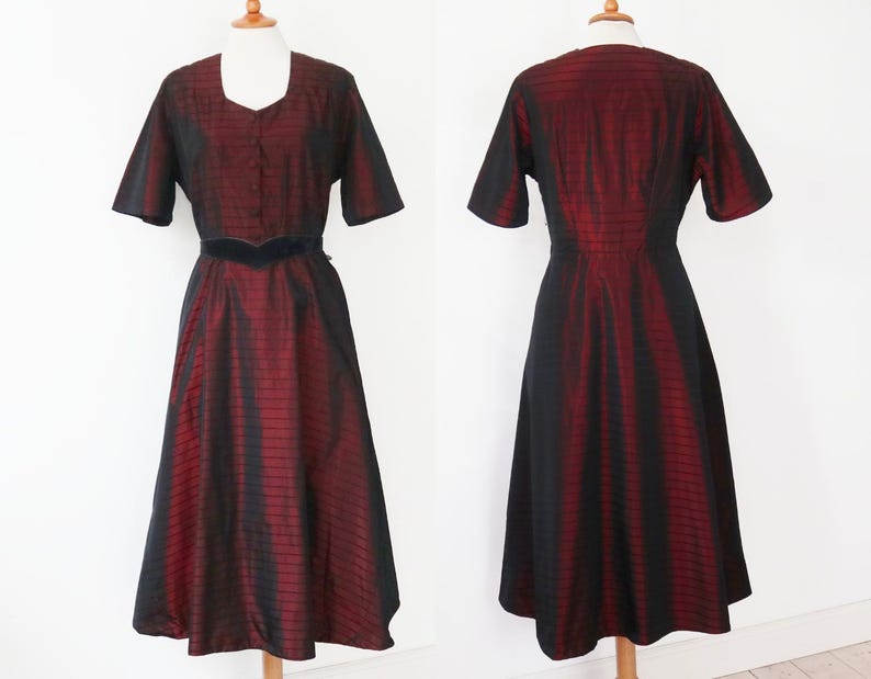 May include: A vintage midi dress in a striking red and black striped pattern. The dress features short sleeves, a square neckline, and a fitted bodice with a defined waist. The skirt flares out, creating an elegant silhouette. The dress is displayed on a mannequin.