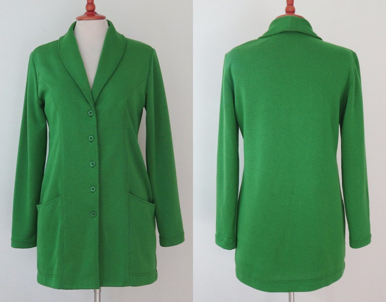 May include: A bright green long-sleeve blazer featuring a shawl collar, five matching green buttons down the front, and two patch pockets. The garment is displayed on a mannequin, showing both the front view with buttons and the plain back view.
