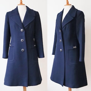 Puede incluir: Un abrigo azul marino de diseño clásico. El abrigo presenta un cuello con solapas, tres botones decorativos y dos bolsillos delanteros. El abrigo se exhibe en un maniquí.