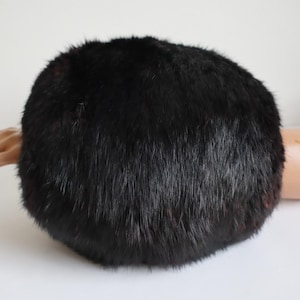 Puede incluir: Un sombrero redondo de piel negra. El sombrero es de un color negro intenso y sólido con una superficie densa y texturizada. El sombrero parece estar hecho de piel suave y es de estilo clásico. Es un accesorio de invierno.