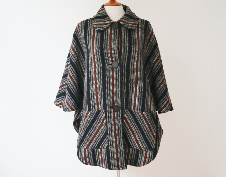 May include: A vintage-style cape coat with a striped pattern in black, gray, and burgundy. The coat features a collar, large buttons, and two front pockets. The cape has a relaxed fit and three-quarter sleeves.