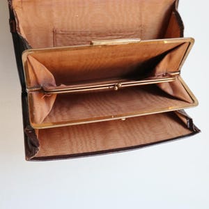 May include: Open vintage brown leather wallet with a gold clasp. The interior features multiple compartments lined with a lighter brown fabric. The wallet is open, showcasing its interior design and construction.