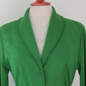 May include: A vibrant green blazer featuring a shawl collar, long sleeves, and a single button closure at the front. The garment is constructed with visible princess seams that extend from the armholes down to the waist, creating a tailored fit.