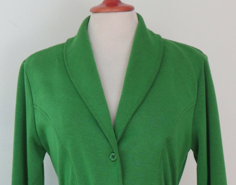 May include: A vibrant green blazer featuring a shawl collar, long sleeves, and a single button closure at the front. The garment is constructed with visible princess seams that extend from the armholes down to the waist, creating a tailored fit.