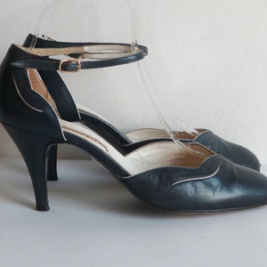 Può includere: Sandali blu navy con tacco alto, cinturino alla caviglia e fibbia dorata. I sandali hanno la punta affilata e un bordo bianco. I tacchi sono alti circa 7.6 cm.