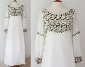 May include: A white vintage dress with a crochet bodice and sheer sleeves. The bodice features a detailed cream-colored crochet design over a dark brown fabric. Green beaded trim accents the neckline and sleeves. The sleeves are long and flowing, with crochet cuffs.