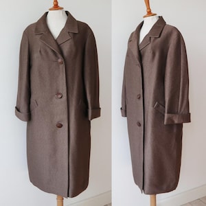 Puede incluir: Un abrigo marrón vintage exhibido en un maniquí. El abrigo presenta un cuello con solapas clásico, cierre de tres botones y mangas con puños. Tiene dos bolsillos delanteros y un corte entallado, mostrando un diseño atemporal.