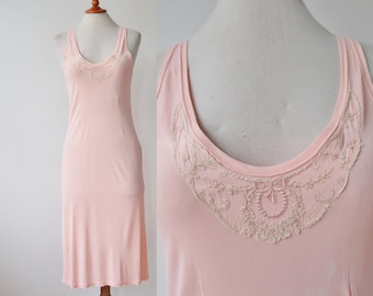 May include: Pale pink slip dress with a scoop neckline and delicate lace trim. The dress is sleeveless and has a simple, elegant design. The lace trim is a lighter shade of pink.