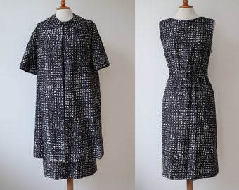 May include: A vintage black and white patterned dress and matching short-sleeved coat displayed on dress forms. The dress is sleeveless with a fitted waist. The coat is knee-length with a collarless design. Both garments have a repeating square pattern.