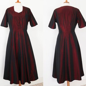 May include: A vintage-style dress in black and red. The dress features a square neckline, short sleeves, and a button-down front. The skirt flares out from the waist. The fabric has a vertical striped pattern.