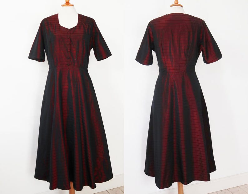 May include: A vintage-style dress in black and red. The dress features a square neckline, short sleeves, and a button-down front. The skirt flares out from the waist. The fabric has a vertical striped pattern.