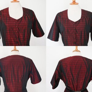 May include: A vintage red and black dress with short sleeves and a square neckline. The dress features a button-down front and a fitted waist. The fabric has a subtle striped pattern. The dress is displayed on a mannequin.