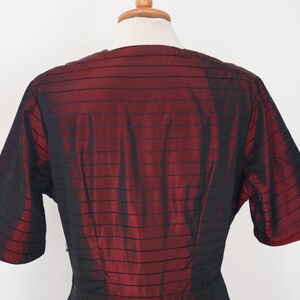 May include: A vintage dress bodice in a rich burgundy and black striped pattern. The short sleeves and V-neckline are visible, showcasing the garment's design. The fabric has a subtle sheen, suggesting a silk or satin material.