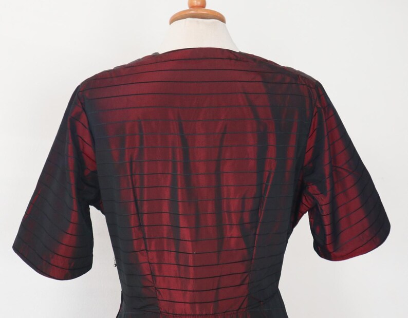 May include: A vintage dress bodice in a rich burgundy and black striped pattern. The short sleeves and V-neckline are visible, showcasing the garment's design. The fabric has a subtle sheen, suggesting a silk or satin material.