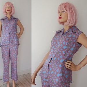 Könnte beinhalten: Ein zweiteiliges Vintage-Outfit mit einem ärmellosen Oberteil mit Kragen und passender Hose. Das Ensemble ist mit einem geometrischen Design in den Farben Mauve, Blau und Grün gemustert. Das Outfit wird auf einer Schaufensterpuppe präsentiert.